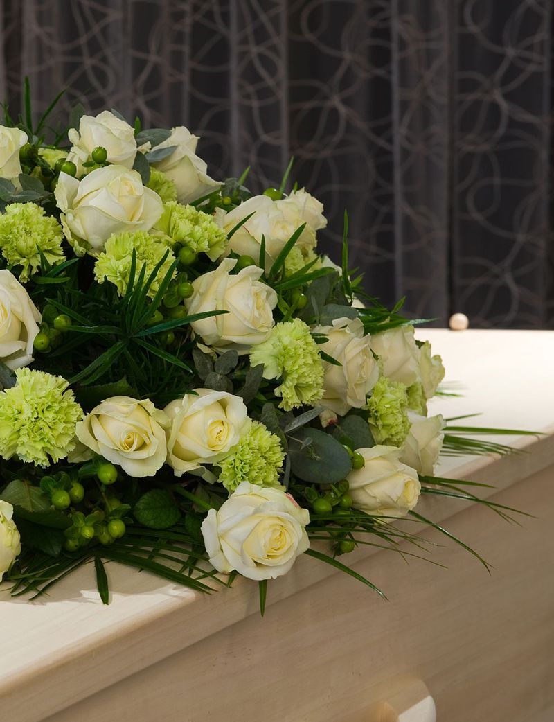 Sarg aus hellen Holz mit weißen Blumen drauf